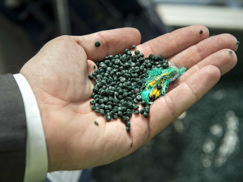 Handgranulate Recyceltes Kunststoffgranulate und ein Stück Fischernetz in einer Hand